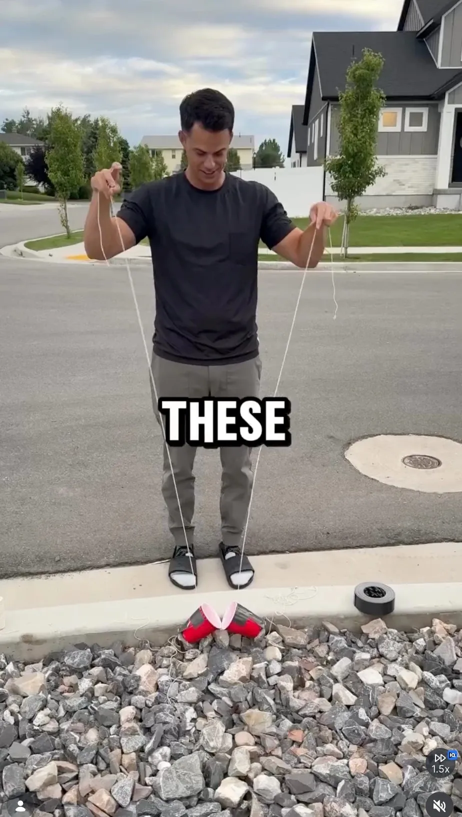 Andy on the curb holding a string rigged to two red cups, about to fish his son's baseball out of a storm drain