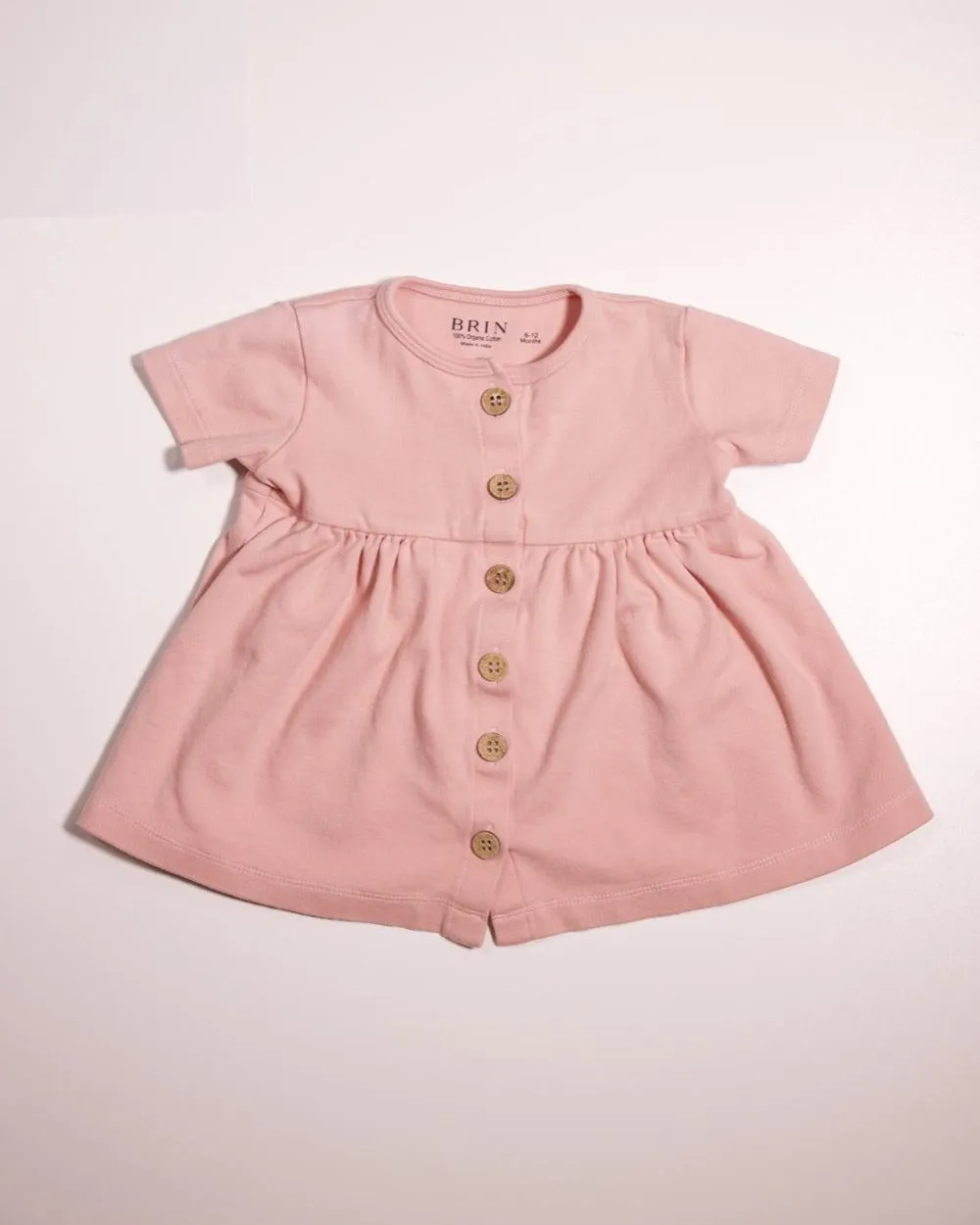 The BRIN Penelope Dress in Rose, laid flat on a white board, photographed at home